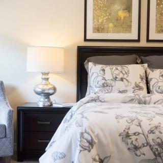 A cozy bedroom with elegant decor, featuring a bed with floral bedding, a nightstand with a lamp, and framed artwork on the wall.