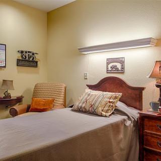 A cozy and inviting bedroom featuring a single bed, a comfortable chair, and warm lighting.