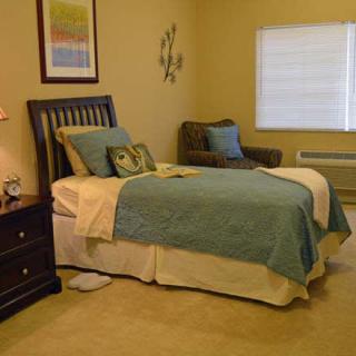 A cozy bedroom with a neatly made bed, cushioned chair, and soft lighting.