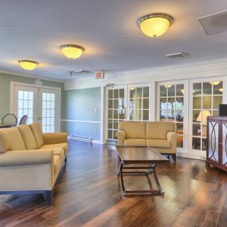 A spacious living room with wooden flooring, featuring sofas, a coffee table, and ample natural light from large windows.