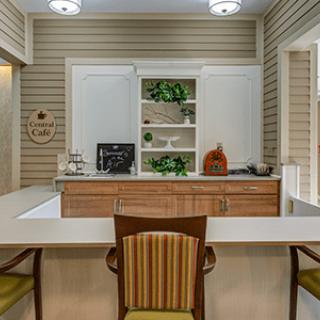 A cozy kitchen interior with a central counter and chairs, featuring decorative shelves.