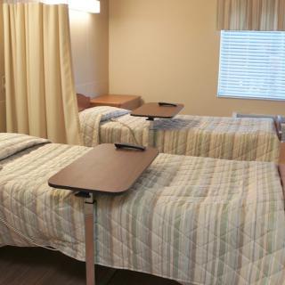 A hospital room with two beds, each equipped with a movable overbed table.