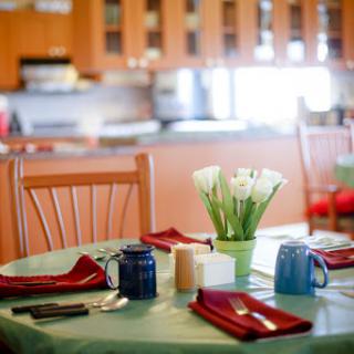 A beautifully set dining table with flowers, utensils, and colorful coffee cups in a cozy kitchen.