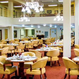 A spacious dining area with multiple tables and chairs, elegantly lit by chandeliers.
