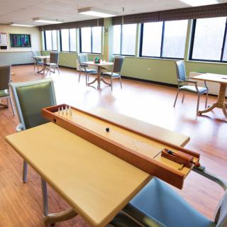 A spacious game room with a shuffleboard table, featuring large windows and multiple seating areas.