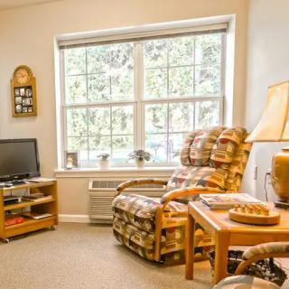 A cozy living room with a large window, an armchair, television, and a lamp on a small table.