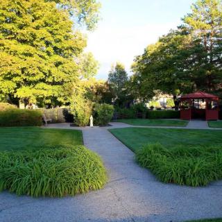 A peaceful park scene with lush greenery and a gazebo in the sunlight.