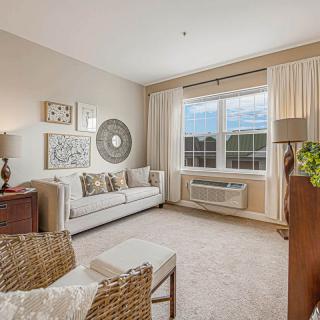 A cozy and elegantly decorated living room with a sofa, artwork, and natural light streaming through a large window.