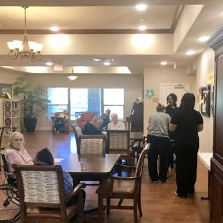 A nursing home common area with residents and caregivers interacting.