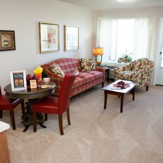 A cozy living room featuring a plaid sofa, an armchair, and a small round dining table with red chairs.