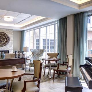 A cozy lounge area with elegant furniture and a piano, bathed in natural light from large windows.