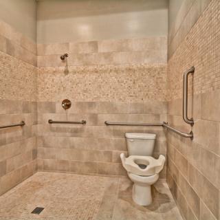 A spacious bathroom with tiled walls, featuring a toilet and shower area equipped with handrails for accessibility.