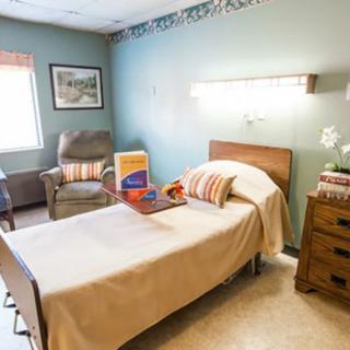A neatly arranged hospital room with a single bed, chair, and window, providing a comfortable environment.