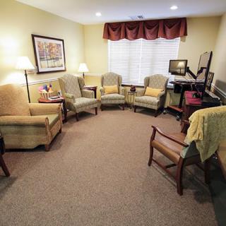 A cozy living room with multiple chairs arranged in a circle, featuring warm lighting and a carpeted floor.