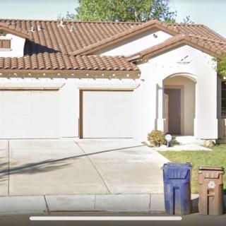 A suburban house with a three-car garage, driveway, and trash bins in front.