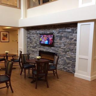 A cozy lobby area features a stone fireplace, a mounted television, and seating arrangements with tables and chairs.