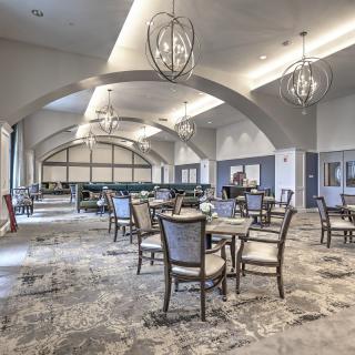 A spacious and elegantly designed dining area featuring modern chandeliers, arched ceilings, and stylish furniture.