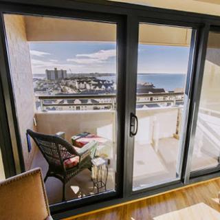 A serene balcony view overlooking the city and ocean, framed by modern glass doors.