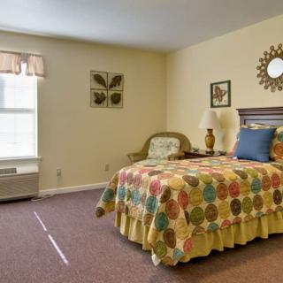 A cozy bedroom with a colorful quilt on the bed, art on the walls, and natural light from a window.