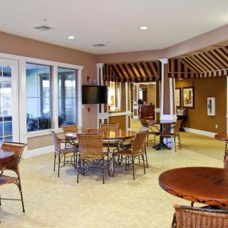 A cozy lounge area with tables and chairs, featuring a large window and a television.