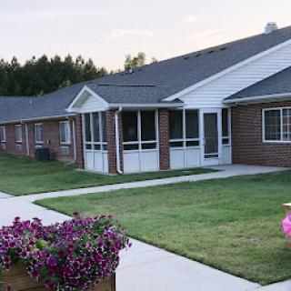 A serene view of a residential building surrounded by lush greenery and colorful flowers.