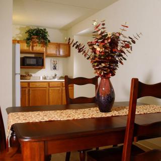 A cozy dining area with a wooden table adorned with a vase of flowers, adjacent to a small kitchen.
