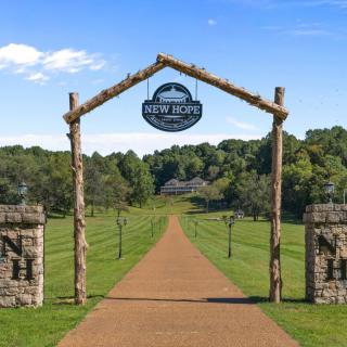 A rustic archway leads into a scenic countryside pathway surrounded by greenery.