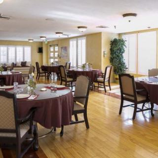 A well-lit dining area with round tables and upholstered chairs on a wooden floor.