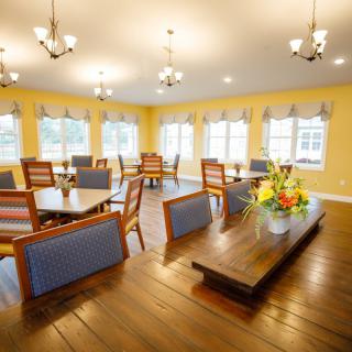 A spacious dining area with wooden floors, colorful chairs, and abundant natural light.