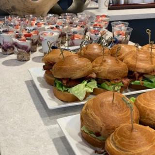 A platter of sandwiches arranged on a buffet table with various appetizers in the background.