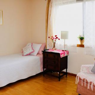 A cozy and minimalist bedroom featuring a single bed, wooden furniture, and soft pink accents.