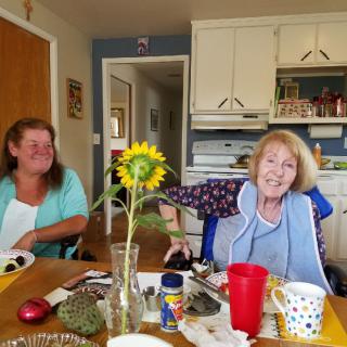 Two women enjoying conversation at a kitchen table with a sunflower centerpiece.