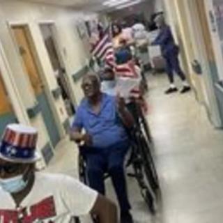 A group of people in wheelchairs adorned with American flags and wearing patriotic hats navigating through a hospital corridor.