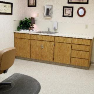 A dental office room featuring a chair, cabinets, and wall decorations.