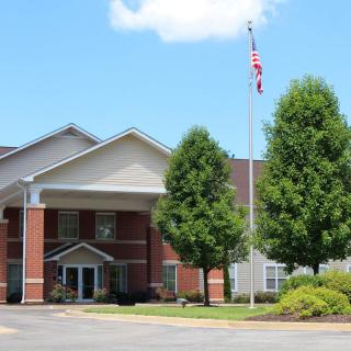 A mid-sized building with a brick facade and a flagpole in front, surrounded by trees under a clear sky.