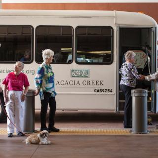 A group of elderly women and a dog in front of an Acacia Creek shuttle bus.