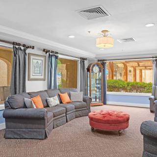 A spacious living room with comfortable sofas, a bright red ottoman, and large windows offering an outdoor view.
