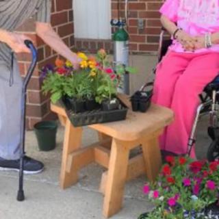 Elderly individuals engaging in gardening activities with flowers, a cane, and a wheelchair present.