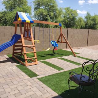 A colorful wooden playground set featuring a slide and swings, nestled in a well-maintained backyard with artificial grass.