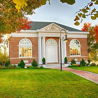 A beautiful brick building with classic columns and a well-maintained green lawn, surrounded by autumn trees.