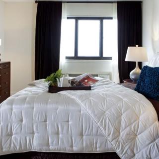 A cozy bedroom with a neatly made bed, featuring white bedding and dark curtains framing the window.