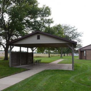 A serene park pavilion surrounded by lush green grass and trees.