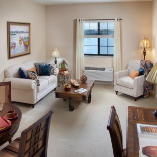 A cozy living room featuring a sofa, armchair, and wooden coffee table with decorative accents, illuminated by soft lighting.
