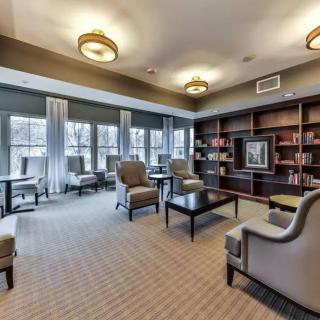 A comfortable lounge area featuring bookshelves, chairs, and large windows.
