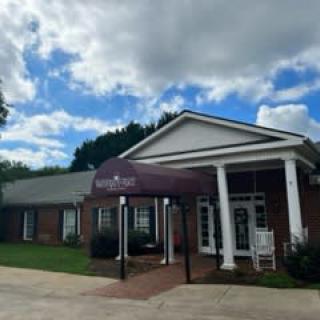 A brick building with a purple awning and white columns under a cloudy sky.