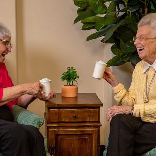 Two elderly women enjoying a joyful moment over drinks, sharing laughter in a cozy indoor setting.