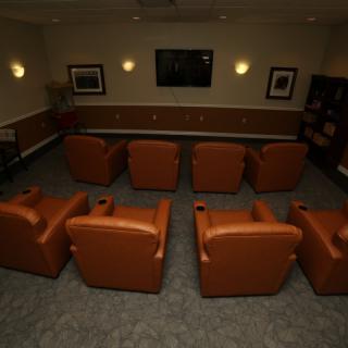 A cozy home theater setup with rows of leather chairs facing a large screen.