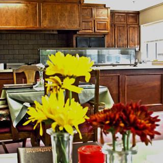 A cozy dining area with vibrant yellow and red flowers in vases on the table, set against a wooden kitchen backdrop.
