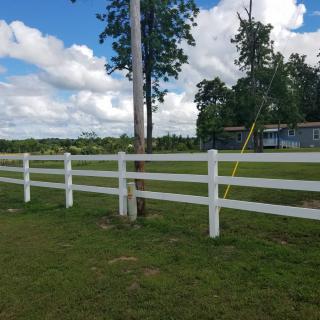 A white fence running alongside a grassy field with trees and a partly cloudy sky.