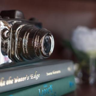 A vintage camera rests atop a stack of books on a shelf.
